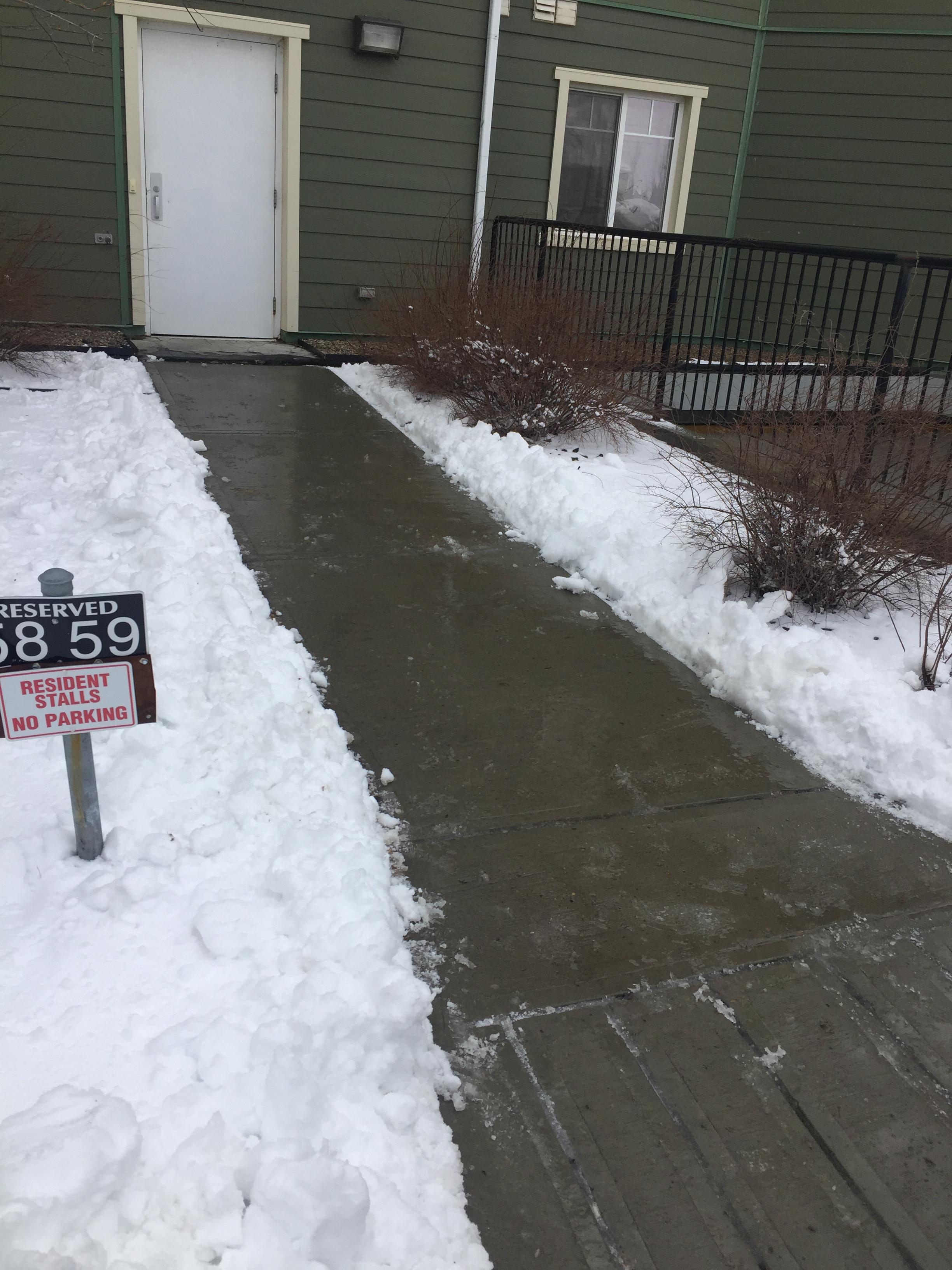 Townhouse walkway cleared with snow banks, reserved parking sign visible